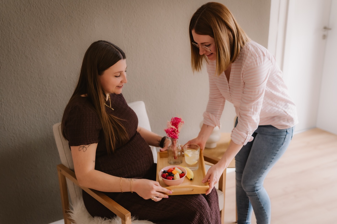Lisa-Marie serviert einer Schwangeren ein Tablett mit Obst und Zitronenwasser